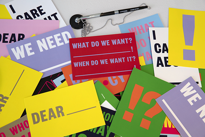 colorful graphic postcards with text like 'WHAT DO WE WANT?—WHEN DO WE NEED IT?'and 'I CARE ABOUT _____' stacked on top of eachother